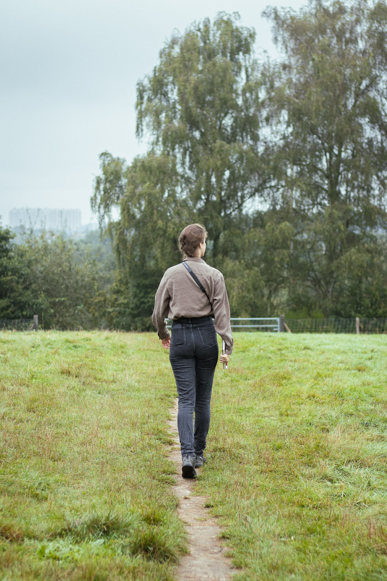 Célestine Merckx de dos, marchant sur un sentier au milieu d'un pré en pleine analyse de terrain